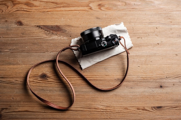 Estilo vintage de câmera digital mirrorless com pulseira de couro isolada em fundo de madeira