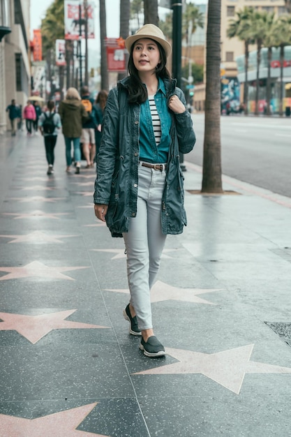 estilo vintage de mochileiro de mulher asiática bonita de comprimento total andando na calçada da fama de hollywood na avenida de hollywood. jovem sorridente viajar em la eua relaxe apreciar a vista da rua na estrada estrela.