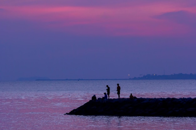 Estilos livres da silhueta da praia do pôr do sol no céu e nas pessoas da água do feriado