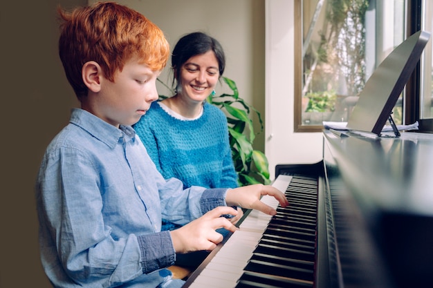 Estilos de vida familiares con niños. Actividades educativas en el hogar. Chico joven de pelo rojo tocando el piano. Niño pequeño que ensaya lecciones de música en un teclado en casa. Estudia y aprende el concepto de carrera musical.