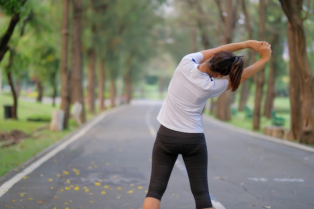 Estiramiento de la mujer de la aptitud en el parque, calentamiento de la hembra listo para correr