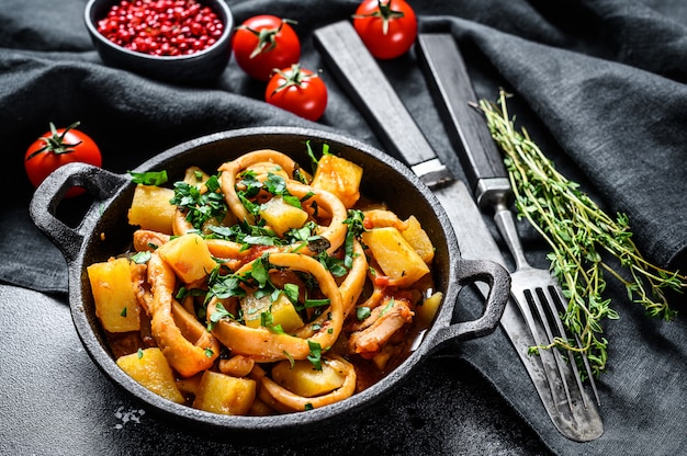 Estofado de calamares, patatas y tomates. Cocina italiana. Fondo negro. Vista superior