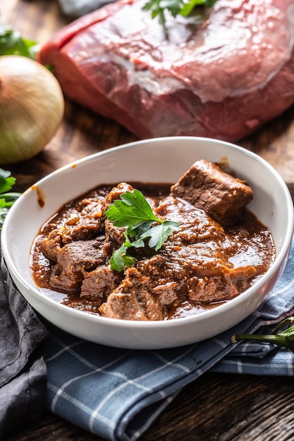 Estofado cocido a fuego lento servido en un plato junto a un trozo de carne cruda de ternera.