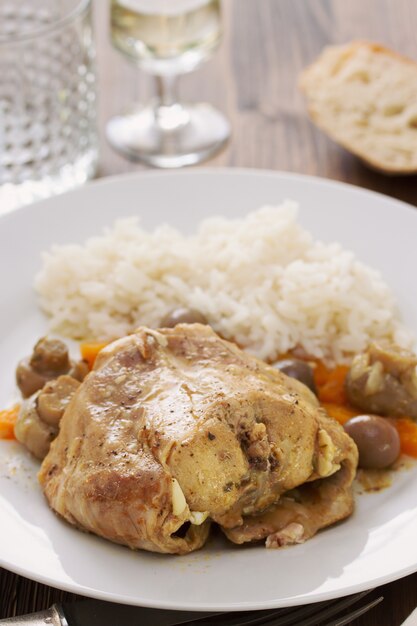 Estofado de conejo con champiñones, zanahoria y arroz hervido en plato blanco sobre mesa de madera marrón