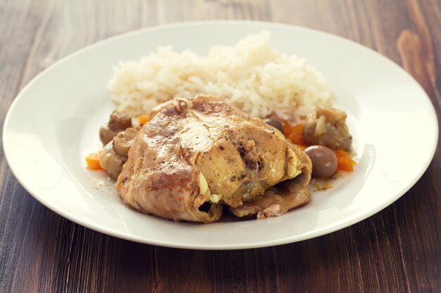 Estofado de conejo con champiñones y zanahoria y arroz hervido en plato blanco sobre mesa marrón