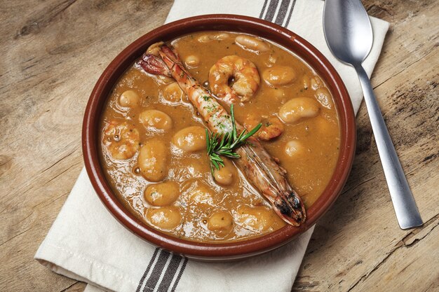 Estofado de judías blancas caseras tradicionales con gambas. Comida típica española. en la mesa de madera