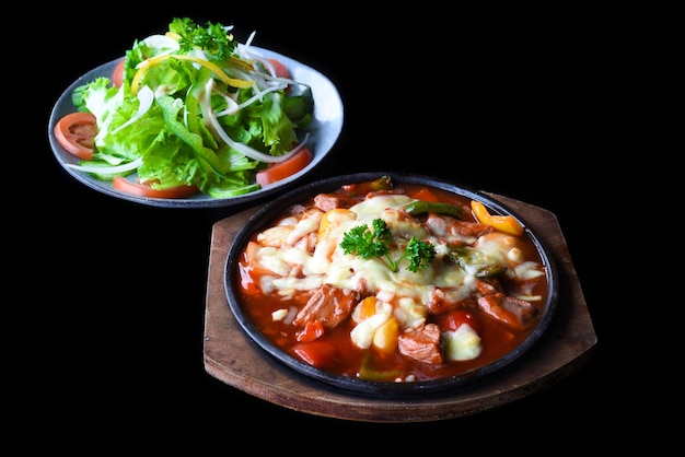 Estofado de ternera con queso y verduras en placa de madera aislado sobre fondo negro