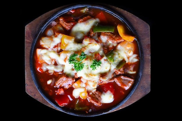 Estofado de ternera con queso y verduras en un plato de madera aislado en la vista superior de fondo negro