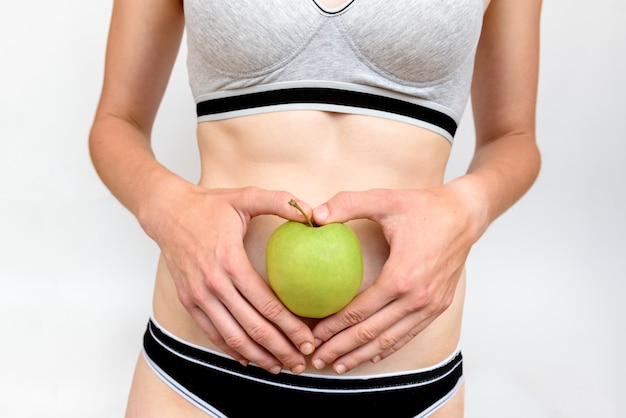 Estômago de mulher com as mãos segurando água e maçã verde sobre fundo cinza. Conceito magro e de dieta.