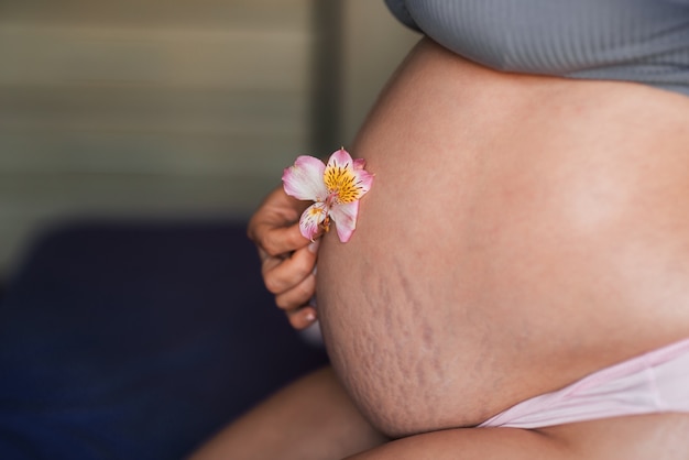 El estómago de la mujer embarazada está cerca con una hermosa flor suave. textura de piel natural de mujer embarazada