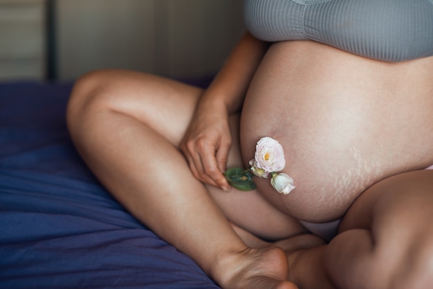 El estómago de la mujer embarazada está cerca con una hermosa flor suave. Textura de piel natural de mujer embarazada