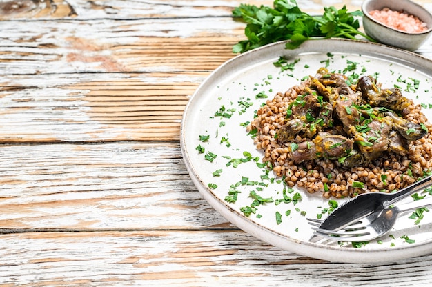 Estómagos de pollo guisados con verduras y trigo sarraceno en un plato. Fondo blanco de madera. Vista superior.