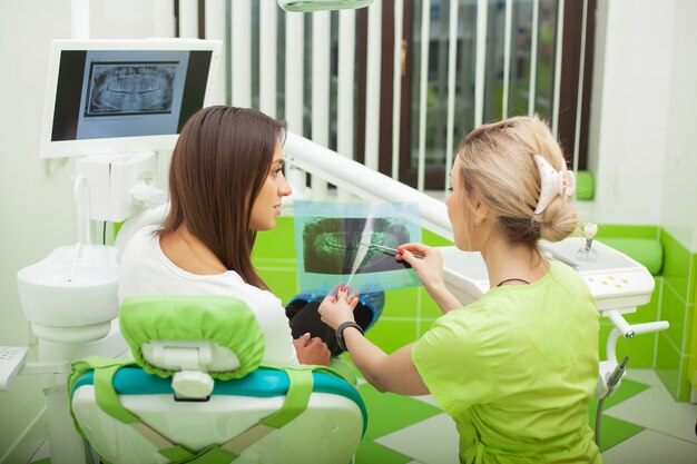 Estomatologista fêmea nas luvas protetoras que examinam os dentes do paciente.