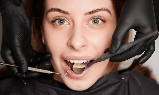 Estomatólogo examinando dientes de mujer con espejo dental y explorador