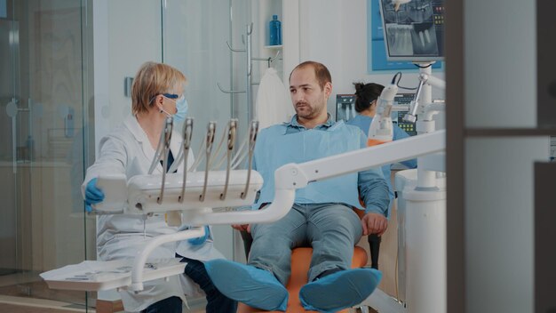 Estomatólogo haciendo un examen dental con herramientas e instrumentos de ortodoncia, tratando al paciente con dolor de muelas. Dentista con taladro y equipo de odontología en el examen de cuidado bucal.