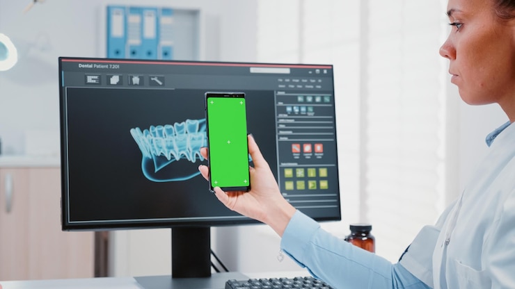 Foto estomatólogo sosteniendo verticalmente la pantalla verde en el teléfono móvil en la oficina del dentista. especialista dental mirando un dispositivo moderno con antecedentes aislados y plantilla de maqueta para el cuidado de los dientes