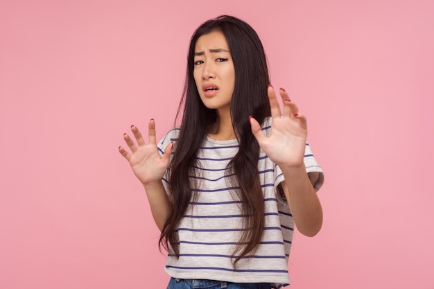 Estou com medo, retrato de menina em pânico com longos cabelos morenos em camiseta listrada, expressando medo, segurando as mãos, parecendo aterrorizado ao perceber algo terrível. tiro de estúdio interno isolado