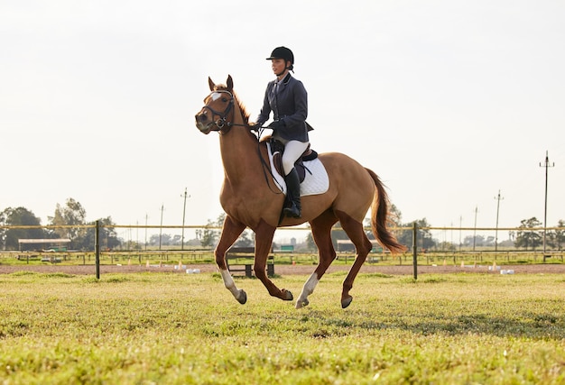 Há uma mulher montando um cavalo pulando sobre um obstáculo