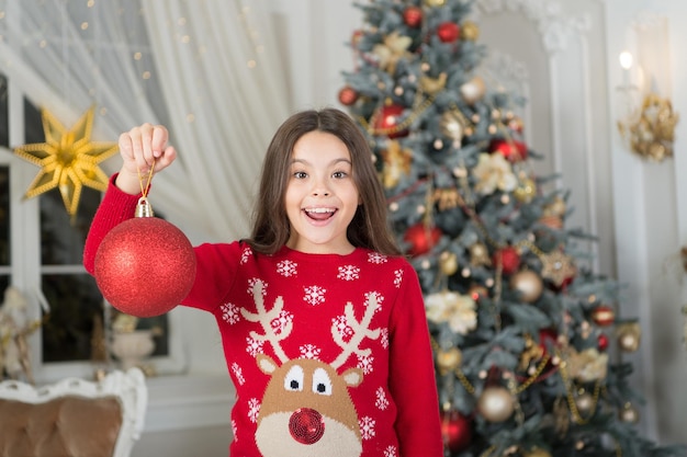 Estou na boa lista do papai noel. garota feliz comemora o natal e o ano novo. menina decorar a árvore de natal. linda garota com bola vermelha. menina pequena aproveite a época festiva. espírito de natal. saudações de ano novo.