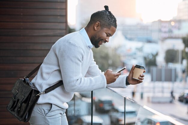 Estou na varanda foto recortada de um jovem empresário bonito mandando mensagens de texto enquanto desfruta de um café para viagem do lado de fora na varanda do escritório