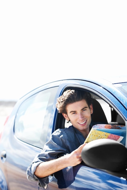 Foto estou no caminho certo jovem sentado em seu carro e sorrindo para a câmera enquanto segura um mapa