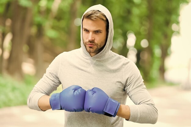 Estou pronto para lutar atleta de homem no rosto concentrado com luvas esportivas praticando fundo de natureza de soco de boxe cabeça de capuz de boxer pronta para lutar treinamento de boxeador esportista com luvas de boxe