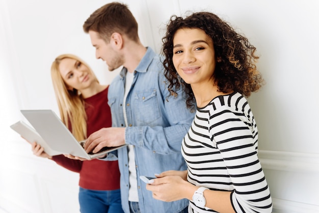 Estoy aquí. Atractiva mujer de pie en posición semi y sosteniendo el teléfono con ambas manos mientras mira hacia adelante