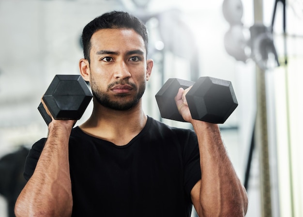 Estoy trabajando duro para lograr mis objetivos de acondicionamiento físico Foto de un apuesto joven haciendo ejercicio con pesas en el gimnasio