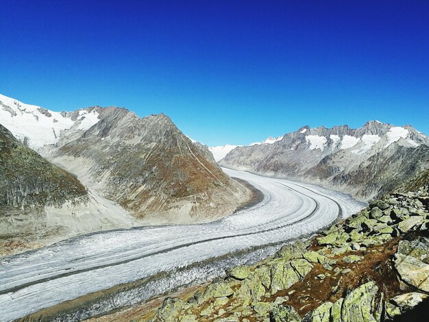 Estrada coberta de neve por montanhas contra um céu azul claro