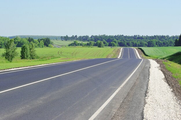 Estrada de asfalto através do campo verde e céu azul em dia de verão