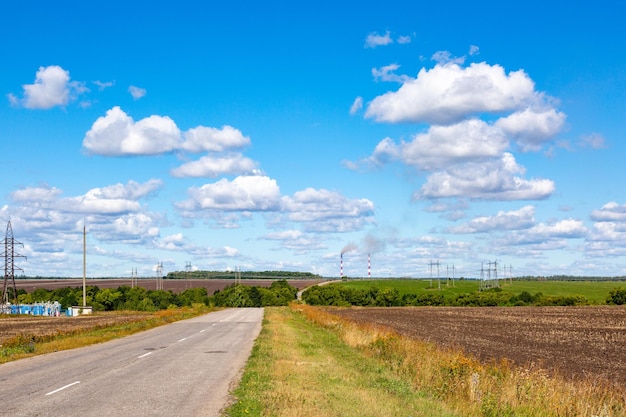 Estrada de asfalto através do campo verde e nuvens no céu azul em dia de verão.