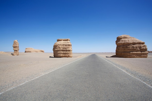 Estrada de asfalto longa e vazia no deserto com forma estranha da pedra e céu azul claro