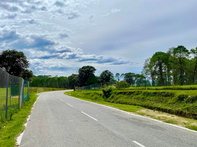 Estrada de asfalto no campo com árvores e céu azul nublado