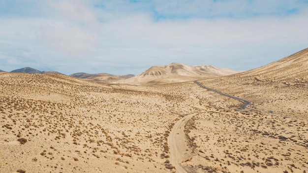 Estrada de caminho no meio de um deserto de areia de montanhas com céu azul brilhante no fundo conceito de desertificação ou mudança climática para o aquecimento global destino de viagem cênico incrível