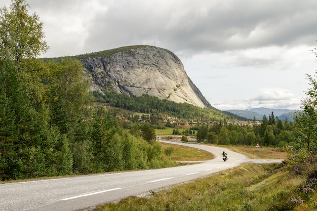 Estrada de montanha com uma motocicleta solitária, dirigindo em direção a uma montanha em setesdal, noruega