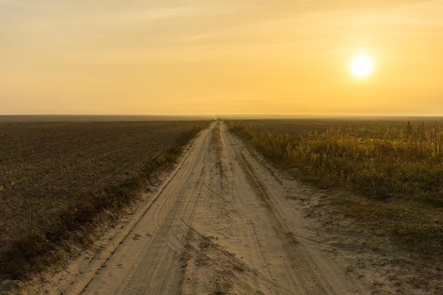 Estrada de terra ao longo do campo e céu amarelo na manhã de outono