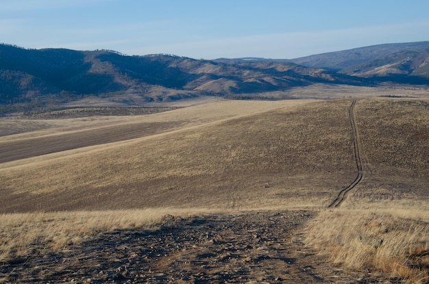 Estrada de terra através das colinas Terreno montanhoso de outono na estepe através da qual a estrada corre