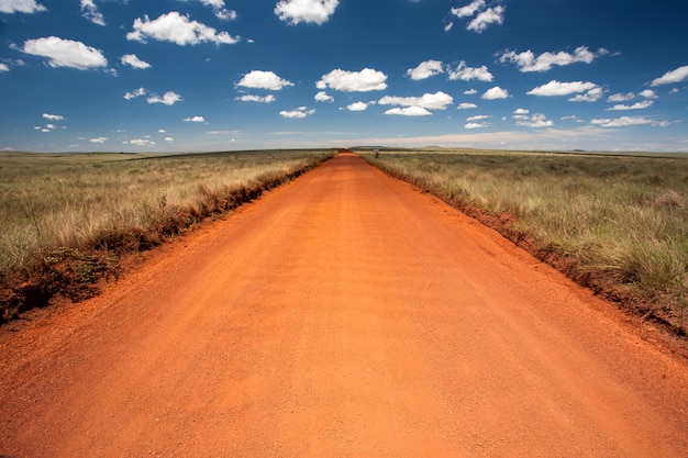 Estrada de terra laranja rural com céu azul e horizonte distante