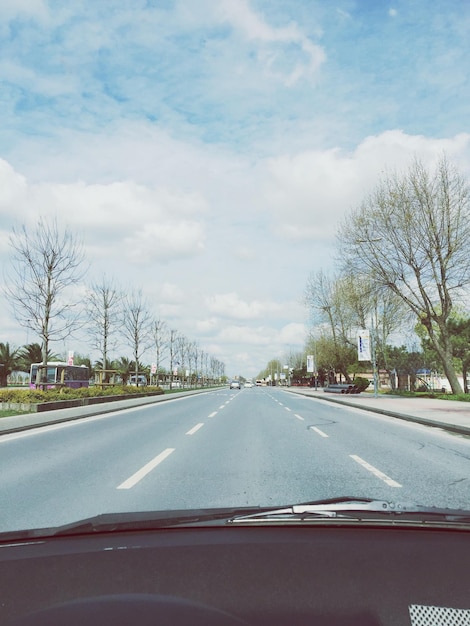 Estrada em meio a árvores contra o céu nublado visto através do pára-brisas do carro