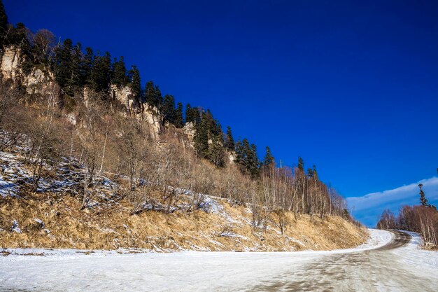 Estrada em montanhas arborizadas no inverno é espalhado com com neve em um dia claro