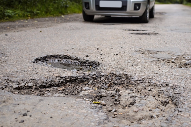 Estrada em péssimas condições, com muitos buracos e buracos e um carro passando por ela