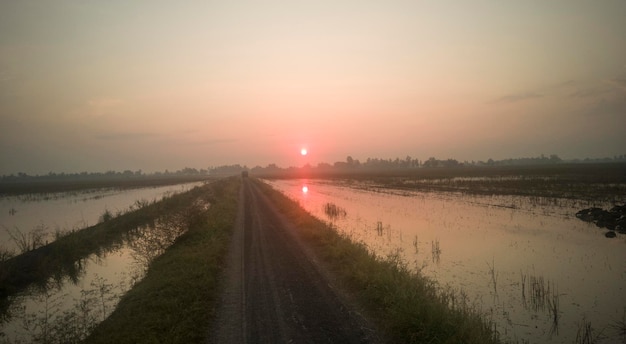 Estrada no meio de um campo agrícola contra o céu durante o pôr-do-sol