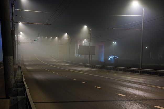 Estrada noturna de neblina vazia iluminada com grades de proteção rígidas