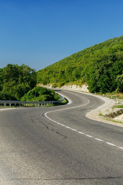 Estrada pavimentada curva fugindo entre montanhas rochosas com árvores verdes