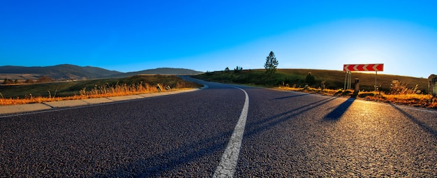 Estrada pavimentada nas montanhas. Paisagem de outono ao pôr do sol.