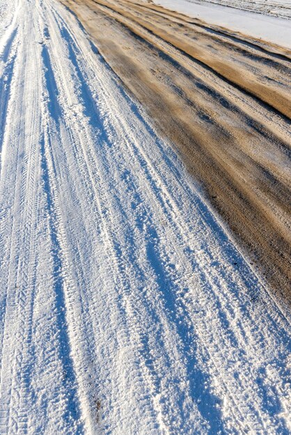 Estrada perigosa na estrada lamacenta escorregadia de inverno com vestígios de carros no inverno após a queda de neve