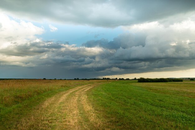 Estrada rural através do prado e nuvem chuvosa no céu