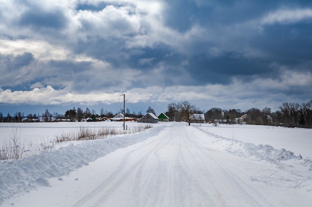 Estrada rural que atravessa os campos até a estrada sSnowy com um céu dramático no inverno