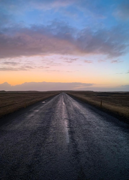 Estrada vazia em meio à terra contra o céu durante o pôr do sol