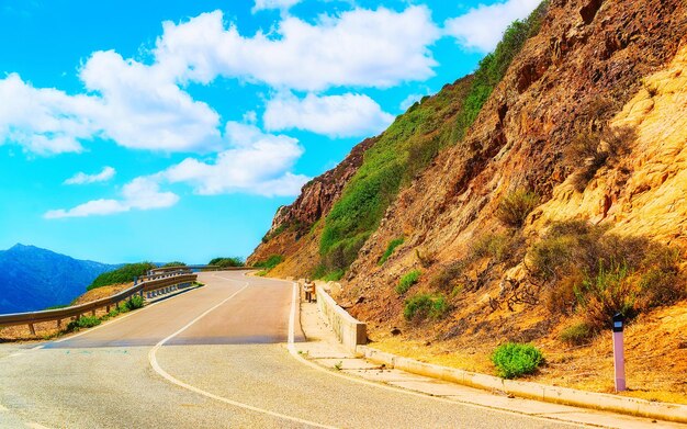 Estrada vazia sem carros em Capo Pecora na ilha da Sardenha no verão de Itália. Transporte de condução na estrada da Europa. Férias na auto-estrada. província de Cagliari. Montanhas no fundo. Mídia mista.